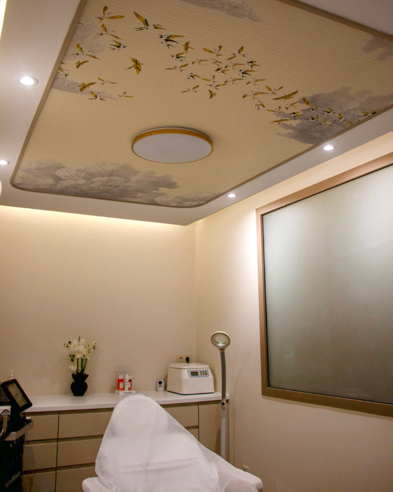 Détail du plafond du cabinet médical : le papier peint aérien est encadré par la plinthe flexible Orac SX194F, formant des courbes continues et fluides. Ce mix papier peint / plinthe crée une transition harmonieuse et souligne la finesse du travail décoratif imaginé par Sarah Khalil.