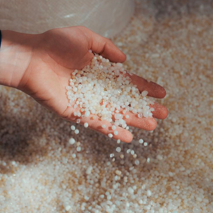 Une main tient des granulés de polymère recyclé, matière première utilisée dans la fabrication des profilés Orac Decor. Cette image illustre l’engagement de la marque pour des matériaux durables et une production respectueuse de l’environnement.